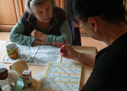 A senior woman and her caregiver work together on a crossword puzzle in a cozy kitchen.